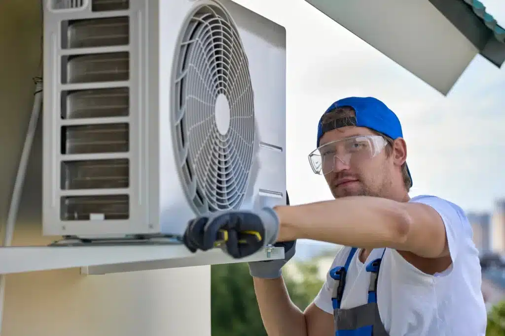 A man in overalls and a hard hat is repairing an air conditioner